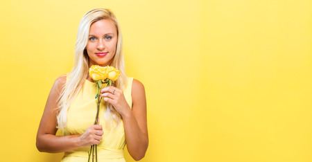 Young woman with flowers on a yellow backgroundの写真素材
