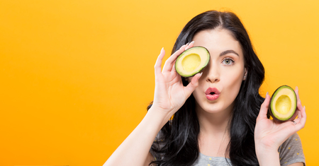 Happy young woman holding avocado halves on a yellow backgroundの写真素材