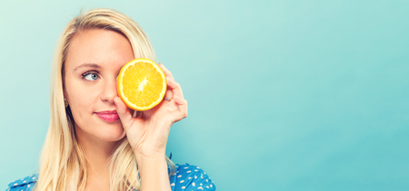 Happy young woman holding a orange halve on a blue backgroundの写真素材