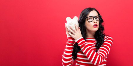 Young woman with a piggy bank on a red backgroundの写真素材