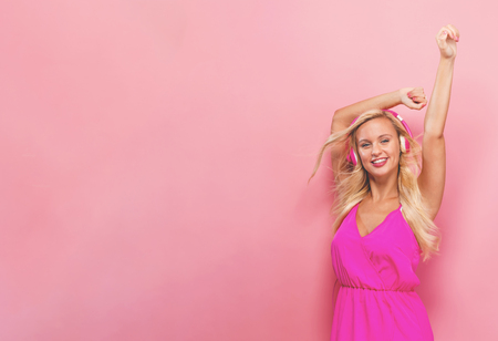 Happy young woman with headphones on a pink backgroundの写真素材