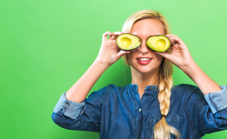 Happy young woman holding avocado halves on a green background
