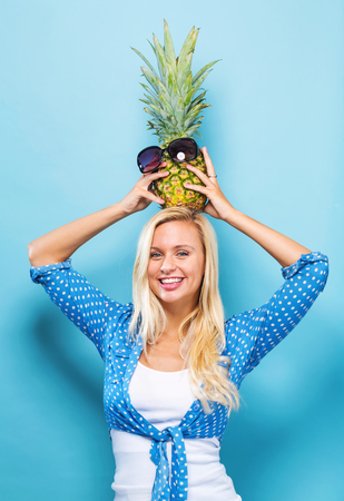 Happy young woman holding a pineapple on a blue backgroundの写真素材