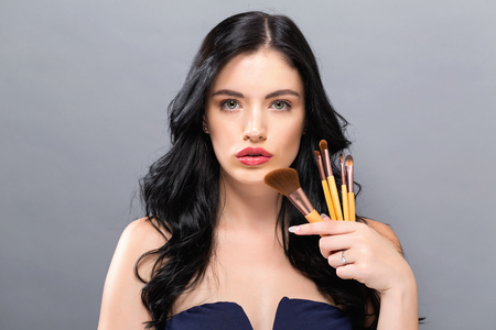 Beautiful young woman holding makeup brushes on a solid backgroundの写真素材