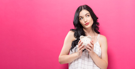 Young woman with a piggy bank on a pink backgroundの写真素材