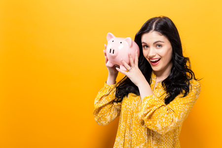 Young woman with a piggy bank on a yellow backgroundの写真素材