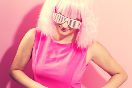 Beautiful woman in a bright pink wig on a pink backgroundの写真素材