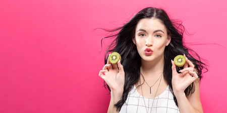 Happy young woman holding kiwis on a pink backgroundの写真素材