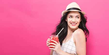 Happy young woman drinking smoothie on a pink backgroundの写真素材