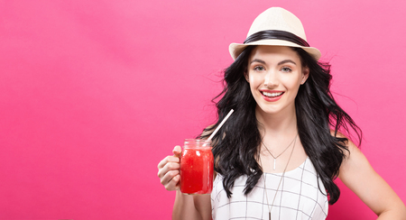 Happy young woman drinking smoothie on a pink backgroundの写真素材