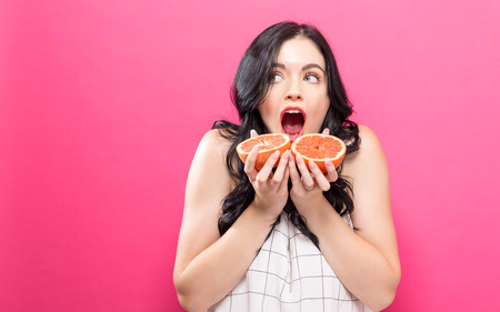 Happy young woman holding oranges on a pink backgroundの写真素材