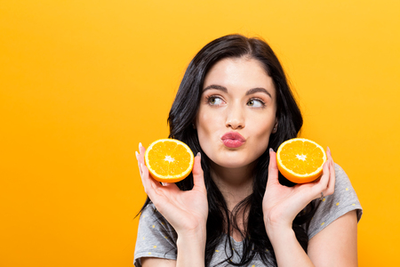Happy young woman holding oranges on a yellow backgroundの写真素材