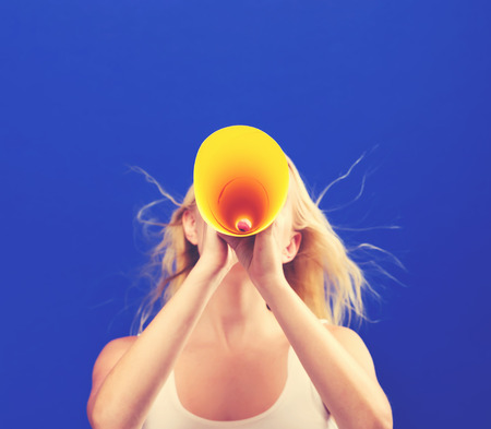 Young woman holding a paper megaphone on a solid backgroundの写真素材