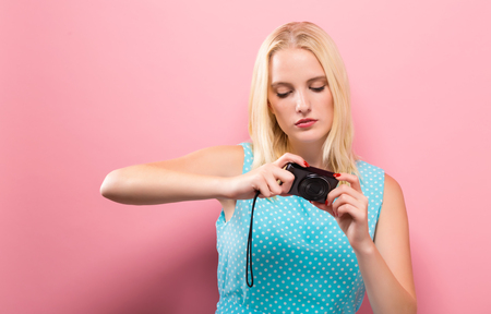 Young woman holding a compact camera on a solid backgroundの写真素材