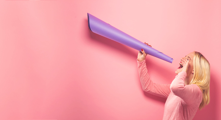Young woman holding a paper megaphone on a solid backgroundの写真素材