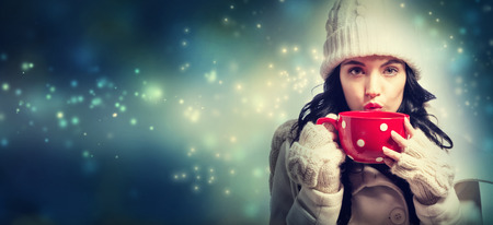 Happy young woman in winter clothes drinking coffeeの写真素材
