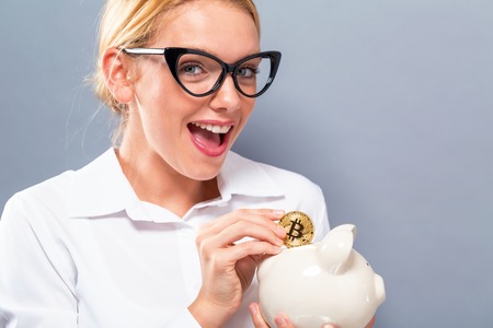 Woman with bitcoin and a piggy bank on a gray backgroundの写真素材