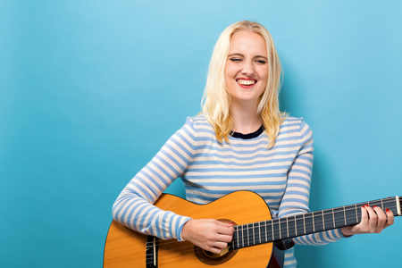 Young woman playing a guitar on a solid background