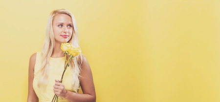 Young woman with flowers on a yellow backgroundの写真素材