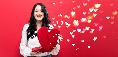 Happy young woman holding a big heart gift box with heart lighsの写真素材