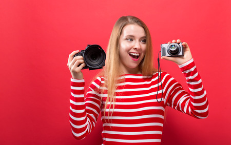 Young woman comparing professional and compact cameras on a solid backgroundの写真素材