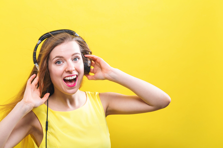 Happy young woman with headphones on a yellow backgroundの写真素材
