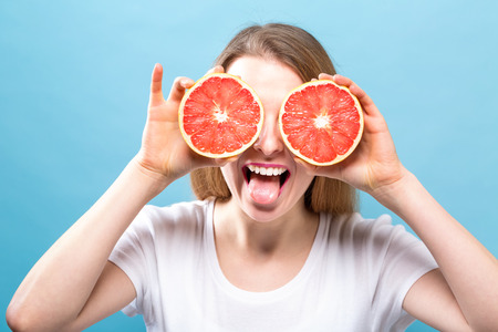 Happy young woman holding grapefruits on a blue backgroundの写真素材