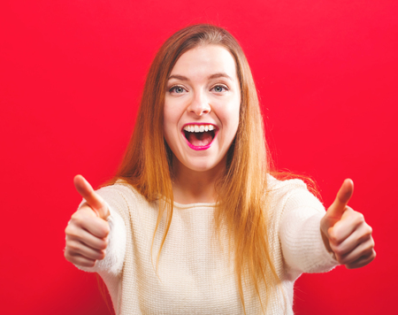 Happy young woman giving thumbs up on a solid backgroundの写真素材