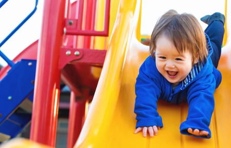 Happy toddler boy playing on a slide at a playgroundの写真素材