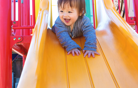 Mixed race toddler boy playing on a slide at a playgroundの写真素材
