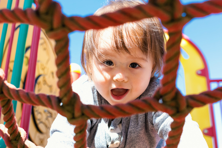 Multracial toddler boy climbing on a playground ropesの写真素材