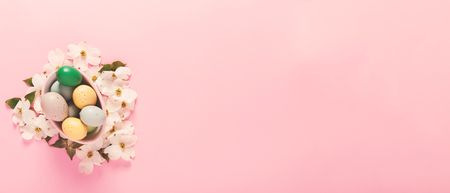 Painted Easter eggs in a basket on a pink background