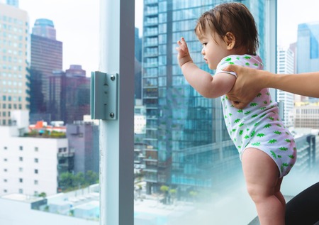 Toddler boy looking out at Downtown Los Angeles from a glass balconyの写真素材