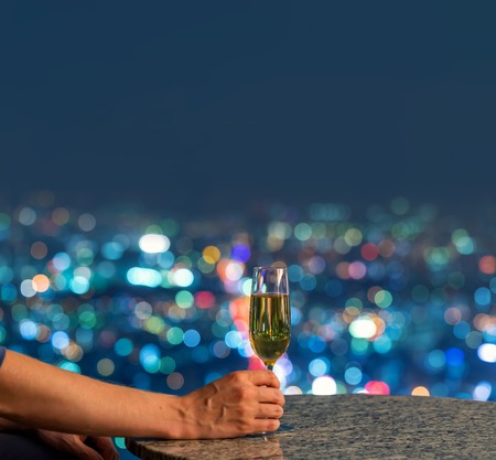 Man with a glass of white wine on a table high above the city at nightの写真素材