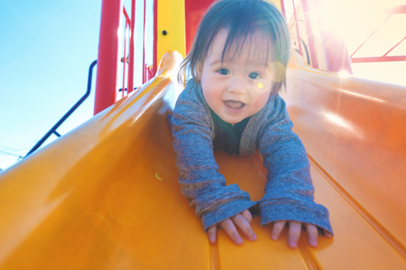 Mixed race toddler boy playing on a slide at a playgroundの写真素材
