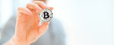 Bitcoin cryptocurrency coin held by a man in a bright room