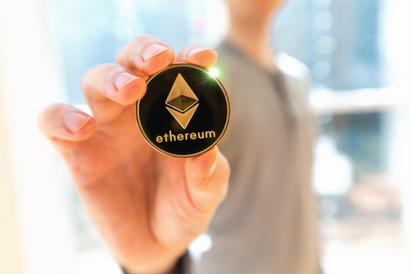 Ethereum cryptocurrency coin held by a man in a bright roomの写真素材