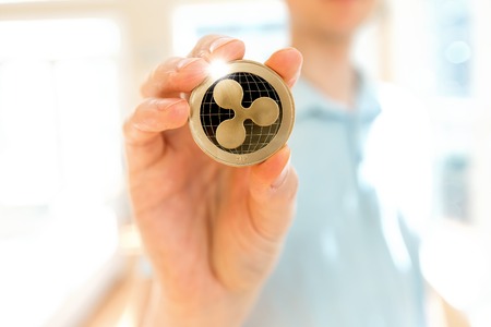 Ripple cryptocurrency coin held by a man in a bright room