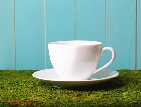 White coffee cup on green grass on a blue background