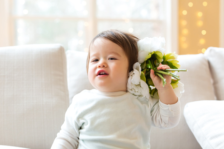 Happy toddler boy playing with flowers in his houseの写真素材