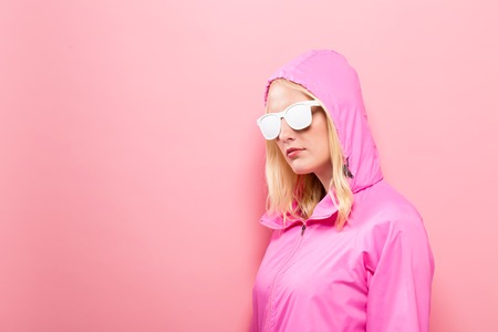 Fashionable woman in pink raincoat and sunglasses on a pink backgroundの写真素材