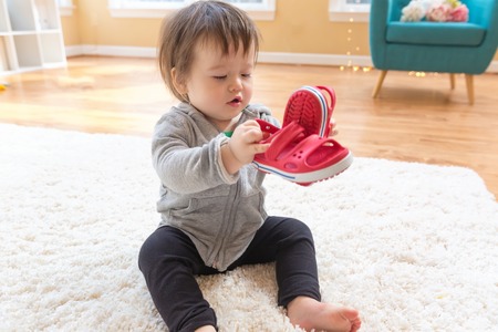 Happy toddler boy playing with his shoes in his houseの写真素材