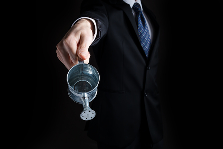 Businessman with watering can concept on a black backgroundの写真素材