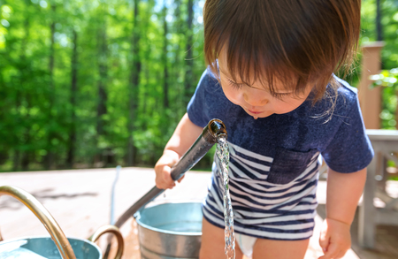 Young toddler boy playing with water from a garden hose outsideの写真素材