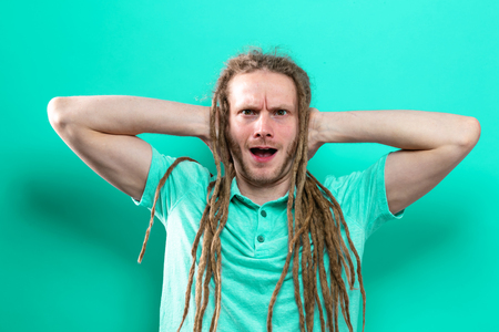 Young man with dreadlocks blocking his ears on a solid backgroundの写真素材