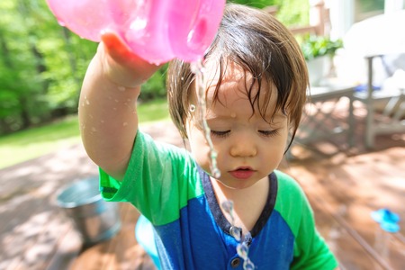 Young toddler boy playing with water outside