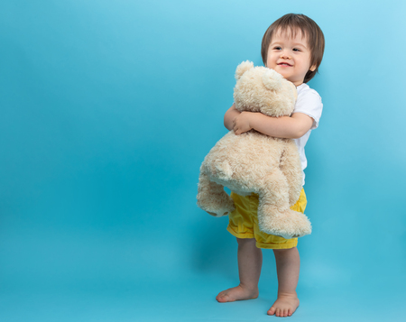 Toddler boy with a teddy bear on a blue backgroundの写真素材