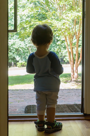 Toddler boy stading in the doorway of his houseの写真素材