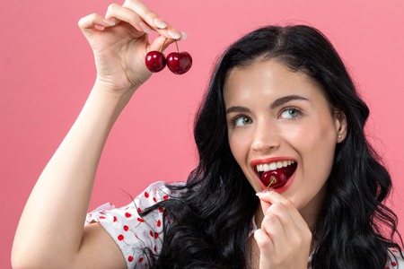 Happy young woman holding cherries on a pink background