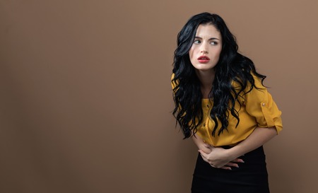 Young woman suffering from stomach pain on a solid backgroundの写真素材